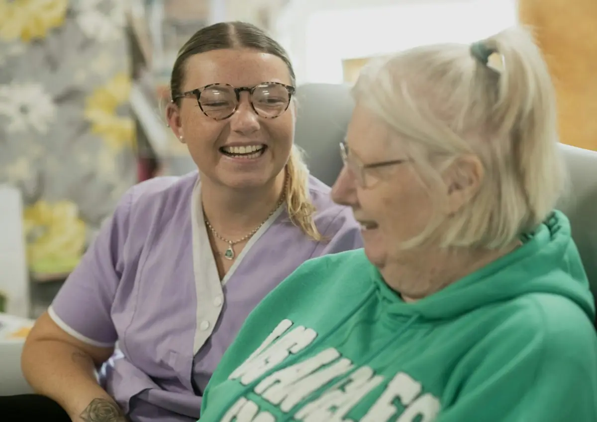 A caregiver and an older woman laughing together